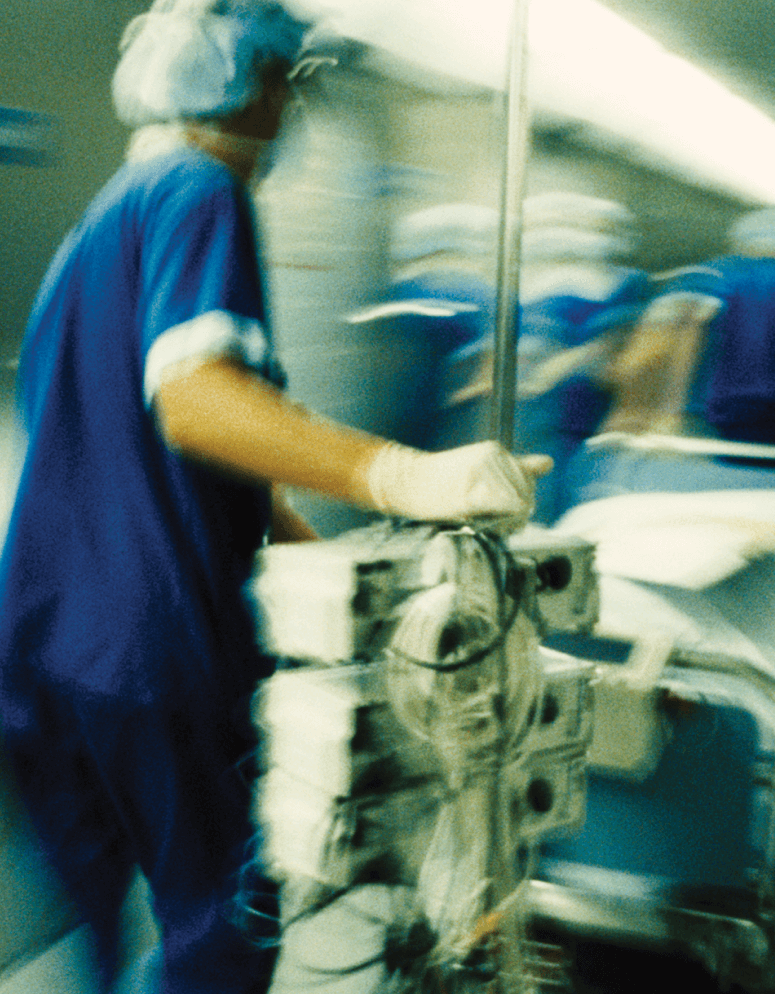 Health care worker pushing patient on gurney down a hallway.