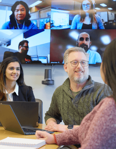 Three OHA staff members gather around a table, with 4 more members are visible on a zoom screen in the meeting room. 