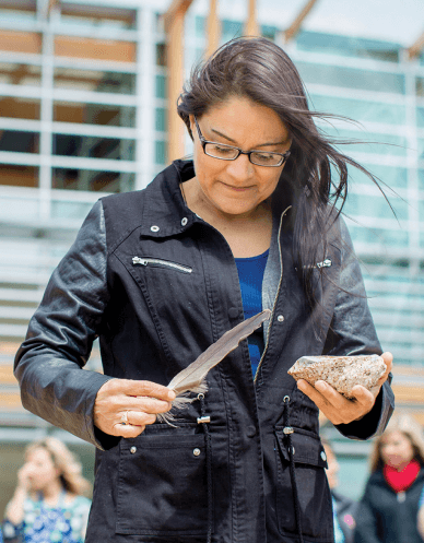 An indigenous woman holds a feather and stone while performing a smudging ceremony. 