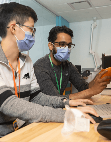 A student and staff member, wearing masks, collaborate over a laptop.  
